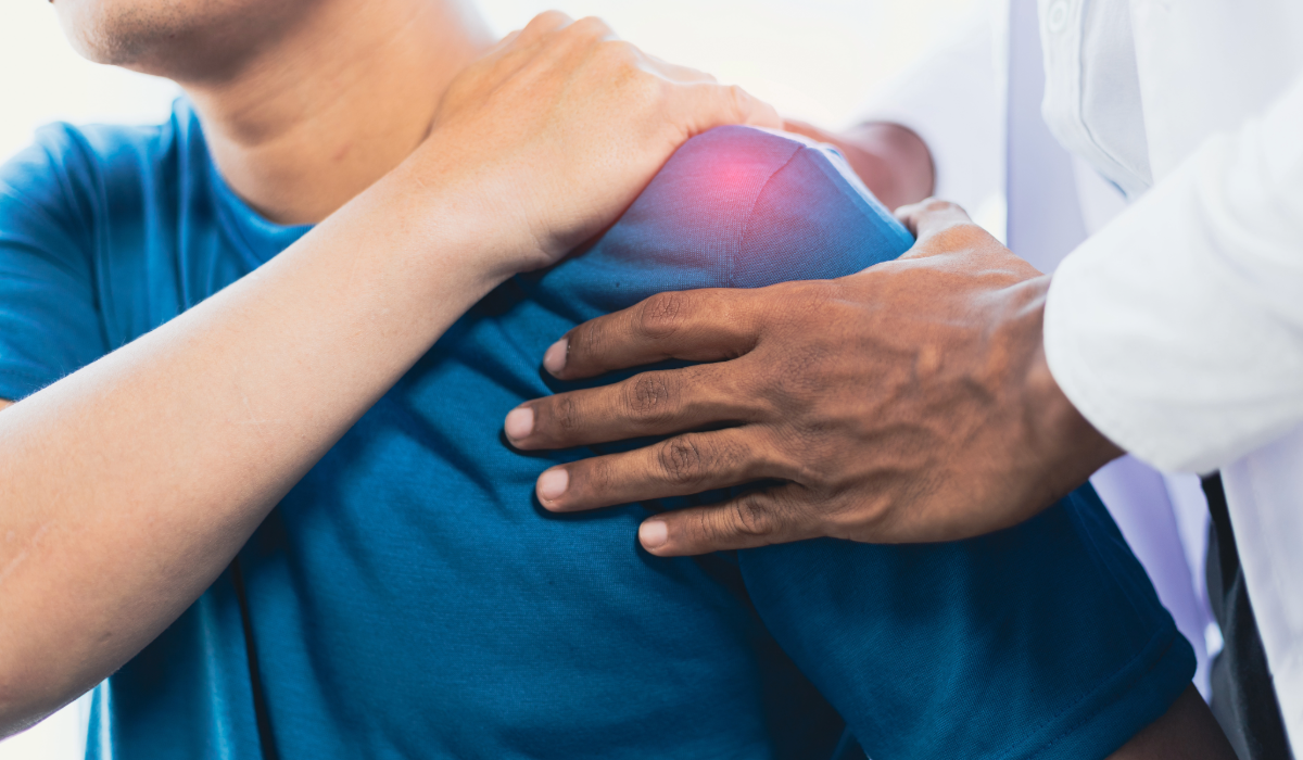 A man holding his left shoulder due to a pain and a clinician holds his shoulder as well