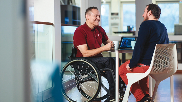 A wheelchair man talking to a colleague at office