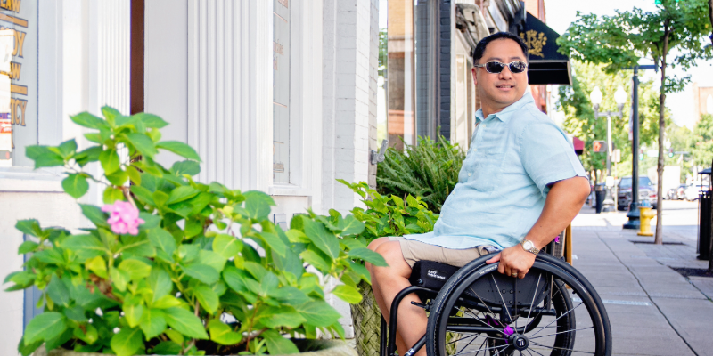 A man on manual wheelchair sitting next to some plants on a street