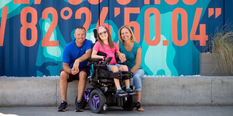 A girl on power wheelchair is with her parents.