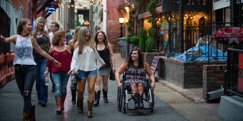 A woman on wheelchair is walking on the street with her friends